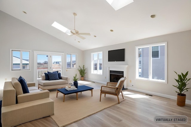 living room featuring visible vents, ceiling fan, light wood-type flooring, a fireplace, and a skylight