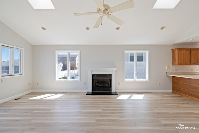 unfurnished living room with a fireplace with raised hearth, vaulted ceiling with skylight, and a healthy amount of sunlight