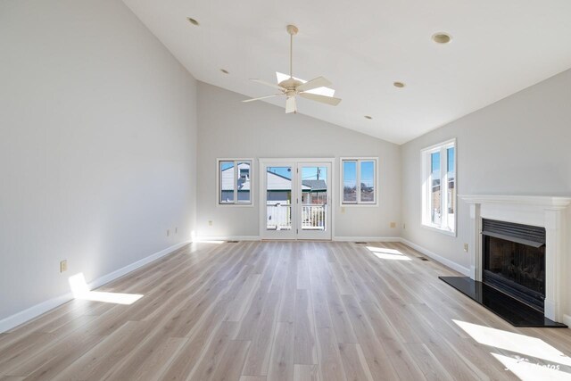 unfurnished living room featuring a fireplace with raised hearth, baseboards, light wood-type flooring, and ceiling fan