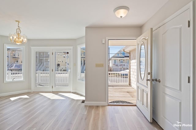 entryway featuring baseboards, light wood-type flooring, and a chandelier