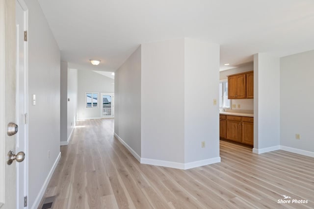 hall with light wood finished floors, a healthy amount of sunlight, and baseboards