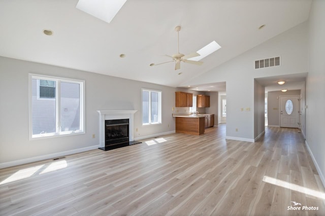 unfurnished living room featuring a skylight, a fireplace with raised hearth, visible vents, and light wood-type flooring