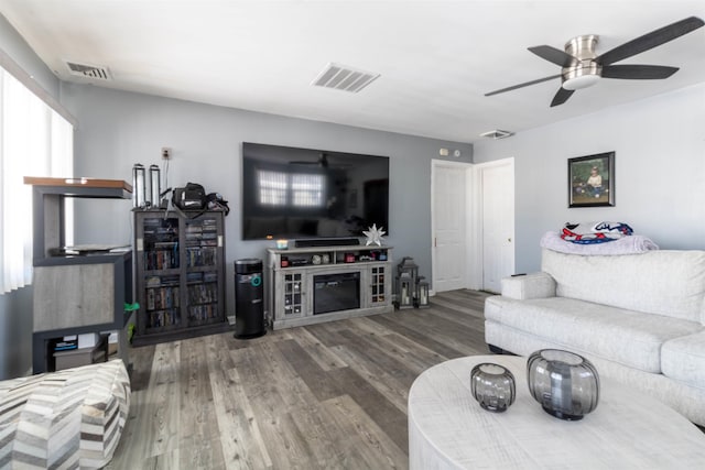 living room with a fireplace, ceiling fan, and wood-type flooring