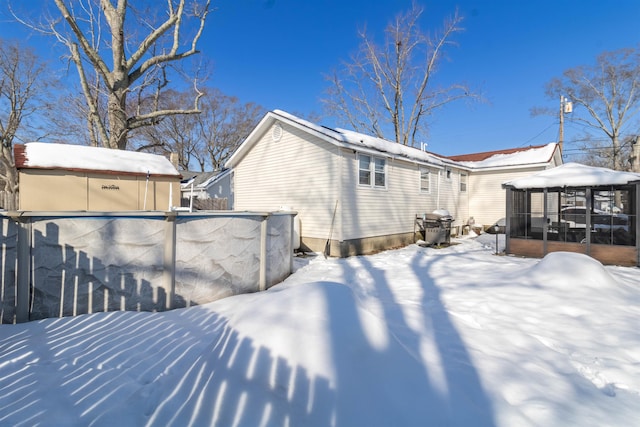 snow covered rear of property with a sunroom