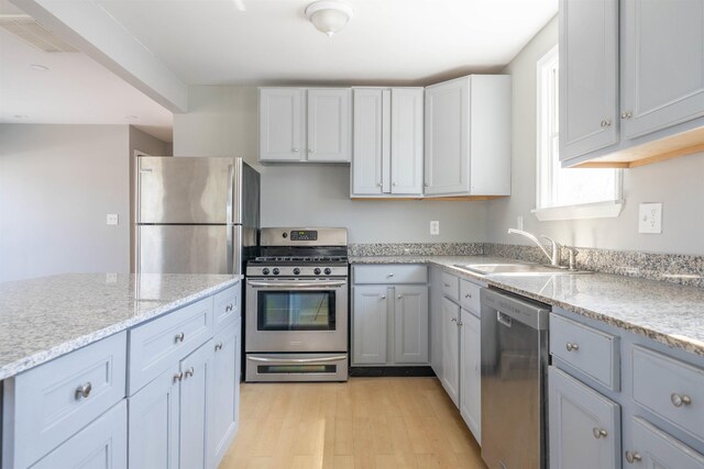 kitchen with a sink, light wood-type flooring, stainless steel appliances, light stone countertops, and visible vents