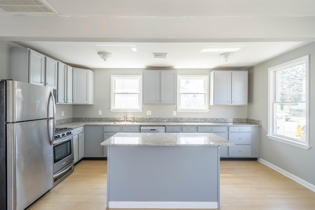 kitchen featuring stainless steel appliances, light wood-style flooring, a sink, visible vents, and light stone counters