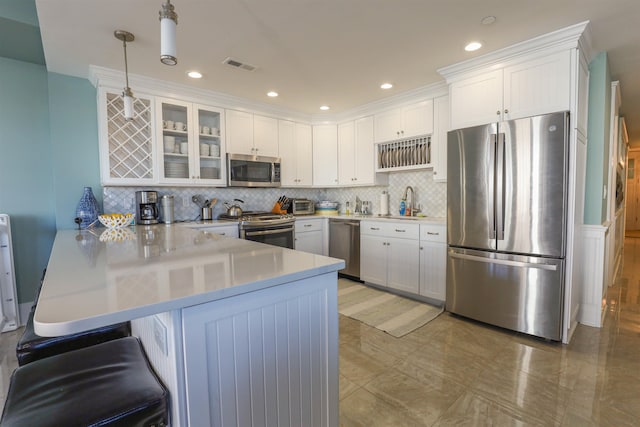 kitchen with kitchen peninsula, hanging light fixtures, decorative backsplash, white cabinetry, and stainless steel appliances