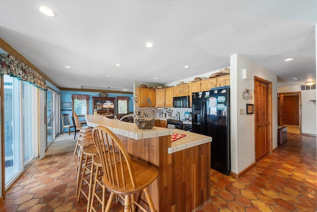 kitchen featuring a kitchen breakfast bar, tile countertops, plenty of natural light, and black appliances