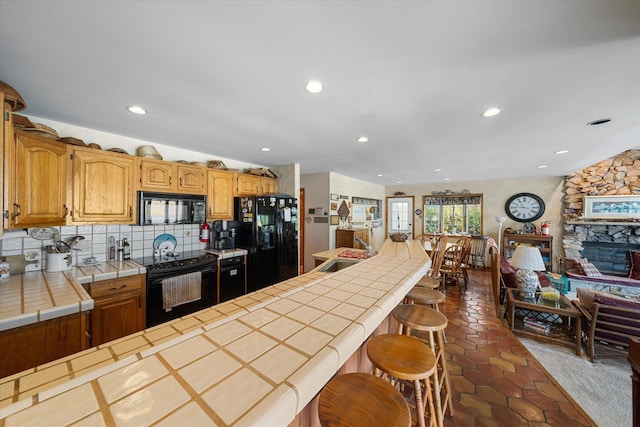 kitchen with tasteful backsplash, a breakfast bar, sink, black appliances, and tile countertops