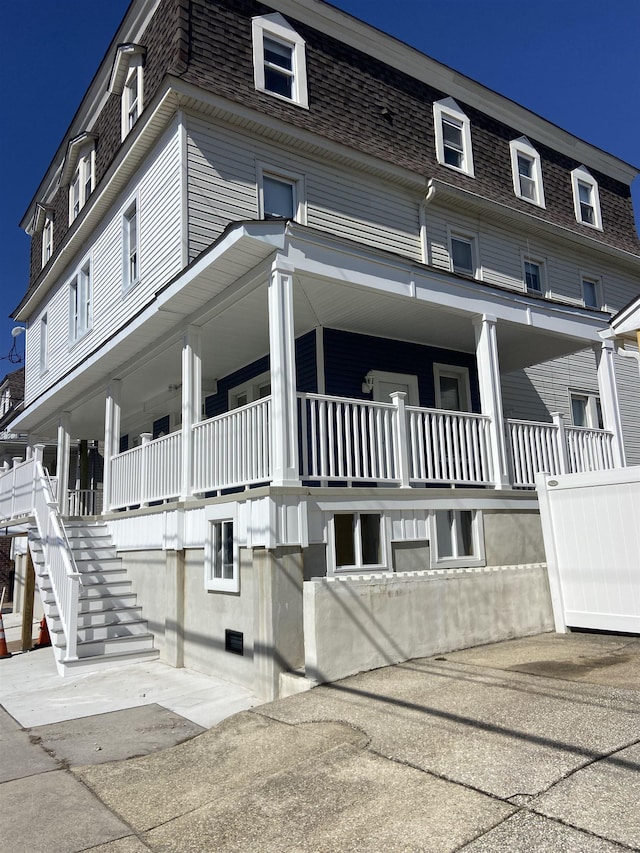 view of front facade featuring a shingled roof, stairs, a porch, and mansard roof