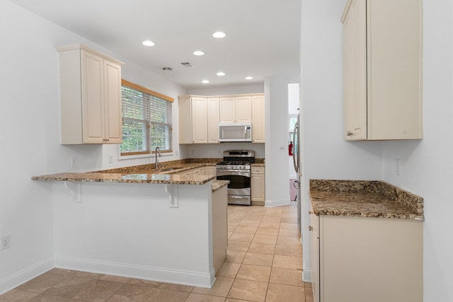 kitchen with dark stone counters, a kitchen breakfast bar, stainless steel gas range, light tile patterned flooring, and kitchen peninsula