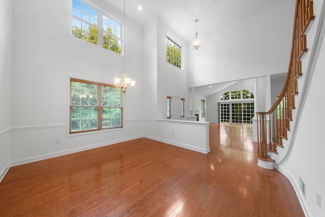 unfurnished living room featuring hardwood / wood-style flooring, plenty of natural light, a high ceiling, and a notable chandelier