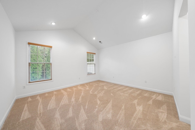 spare room with light carpet, plenty of natural light, and vaulted ceiling