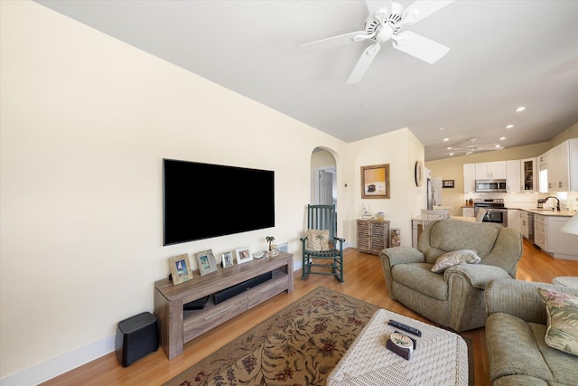 living room featuring ceiling fan, sink, light hardwood / wood-style floors, and vaulted ceiling