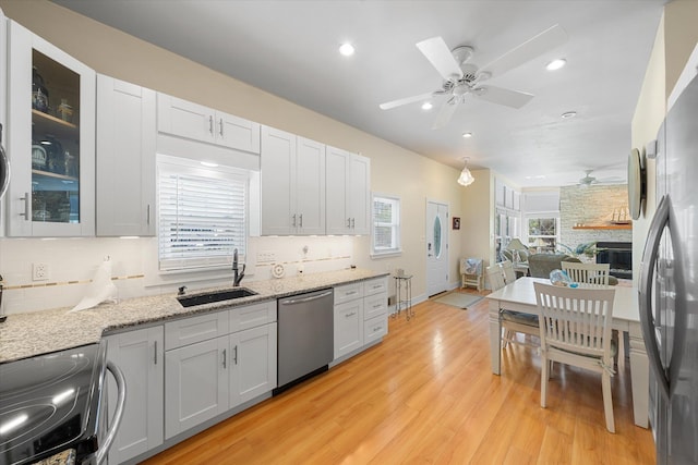 kitchen featuring light stone counters, stainless steel appliances, sink, light hardwood / wood-style floors, and a stone fireplace