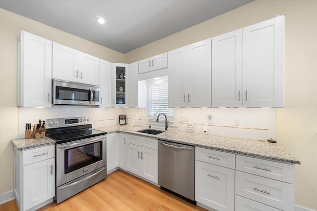 kitchen featuring light stone countertops, white cabinetry, sink, stainless steel appliances, and light wood-type flooring