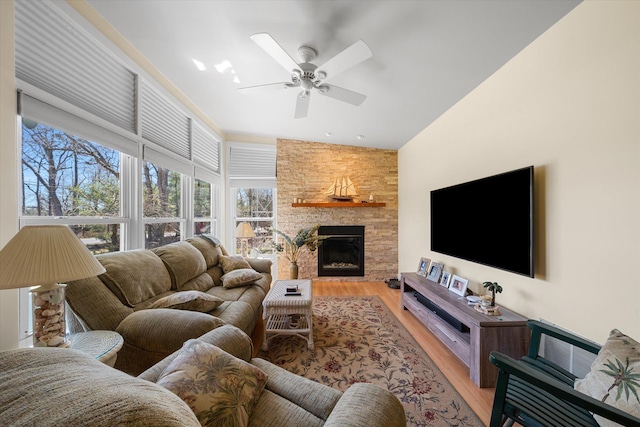 living room featuring a stone fireplace, ceiling fan, and light wood-type flooring