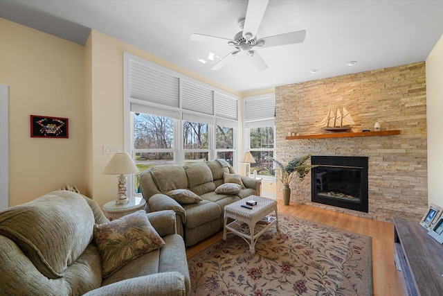 living room with ceiling fan, a stone fireplace, and wood-type flooring