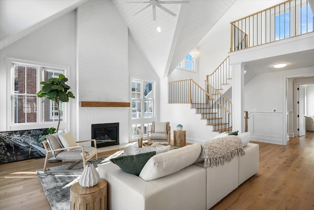 living room with ceiling fan, a brick fireplace, high vaulted ceiling, and light hardwood / wood-style flooring