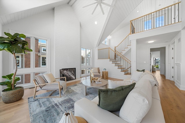 living room featuring high vaulted ceiling, a large fireplace, wood ceiling, light hardwood / wood-style floors, and beam ceiling