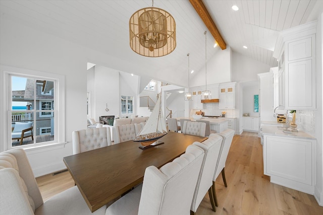 dining space with beam ceiling, high vaulted ceiling, light hardwood / wood-style flooring, and a notable chandelier