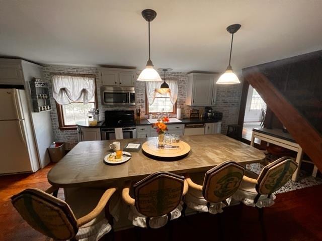 kitchen with sink, hanging light fixtures, white fridge, range, and brick wall