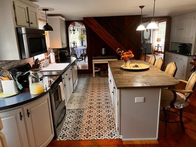 kitchen featuring a breakfast bar, decorative light fixtures, stainless steel appliances, and white cabinets