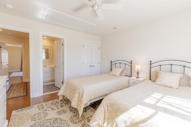 bedroom with attic access, wood finished floors, a closet, ensuite bath, and a ceiling fan