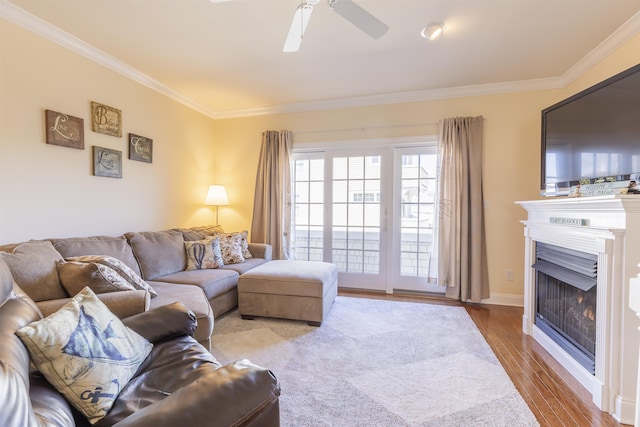 living room featuring a ceiling fan, a lit fireplace, wood finished floors, and crown molding