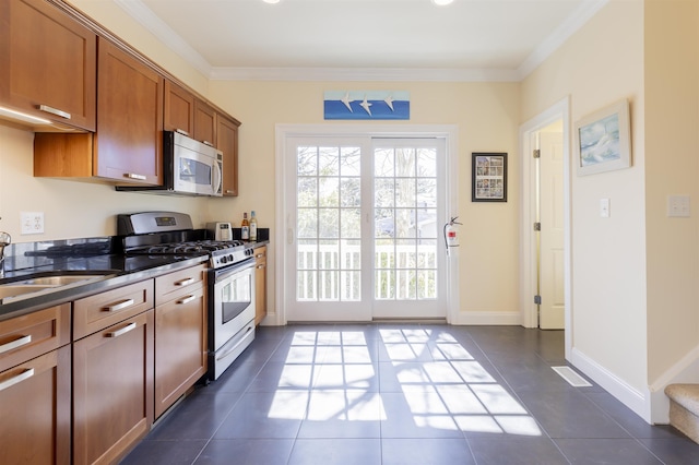 kitchen with dark countertops, ornamental molding, brown cabinets, stainless steel appliances, and a sink