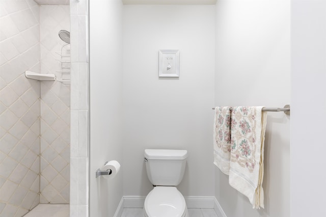 bathroom with tile patterned flooring, toilet, baseboards, and tiled shower