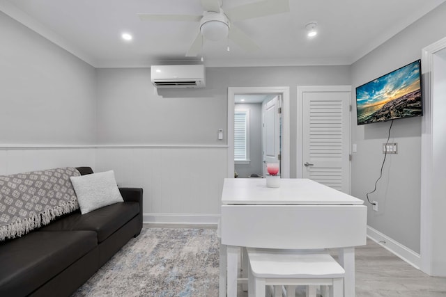 living room featuring ceiling fan, wainscoting, a wall mounted air conditioner, ornamental molding, and light wood-style flooring