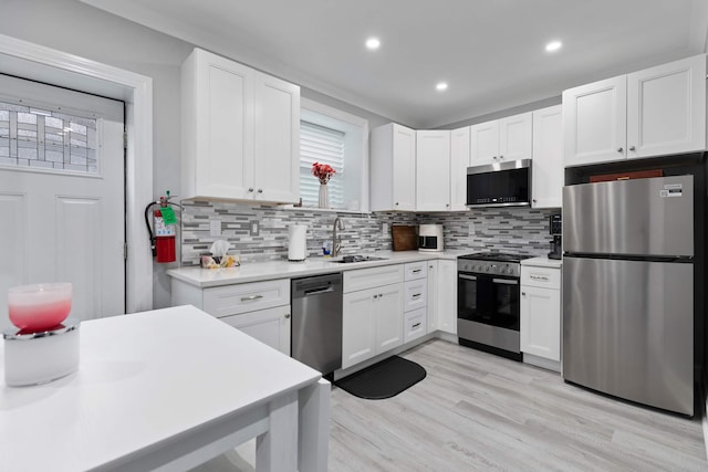 kitchen featuring white cabinets, appliances with stainless steel finishes, a sink, light countertops, and tasteful backsplash