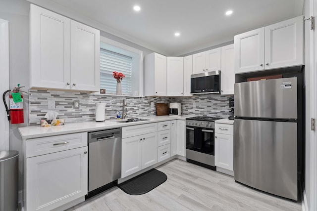 kitchen featuring light countertops, white cabinets, a sink, light wood finished floors, and stainless steel appliances