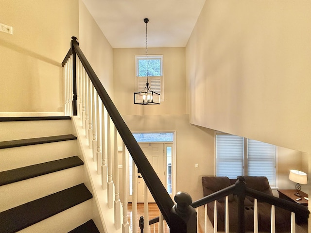 staircase with a chandelier, a towering ceiling, and wood finished floors