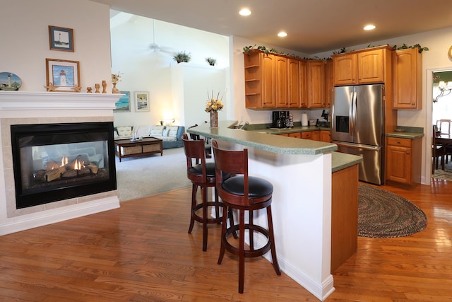 kitchen featuring light hardwood / wood-style flooring, a breakfast bar area, kitchen peninsula, and stainless steel fridge with ice dispenser