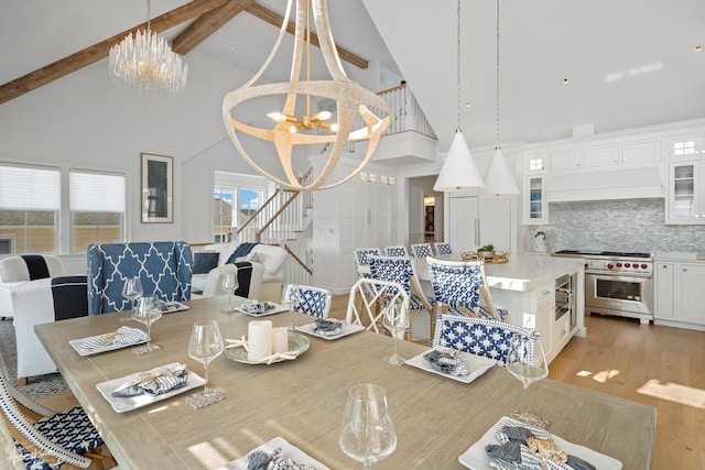 dining area with high vaulted ceiling, beam ceiling, stairs, light wood-type flooring, and a chandelier