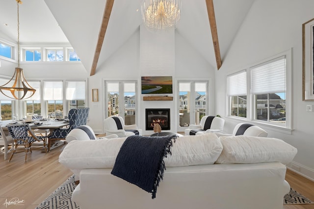 living area featuring baseboards, light wood finished floors, high vaulted ceiling, a large fireplace, and a chandelier