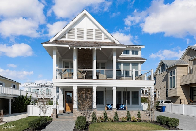 view of front of house with brick siding, covered porch, a balcony, and fence