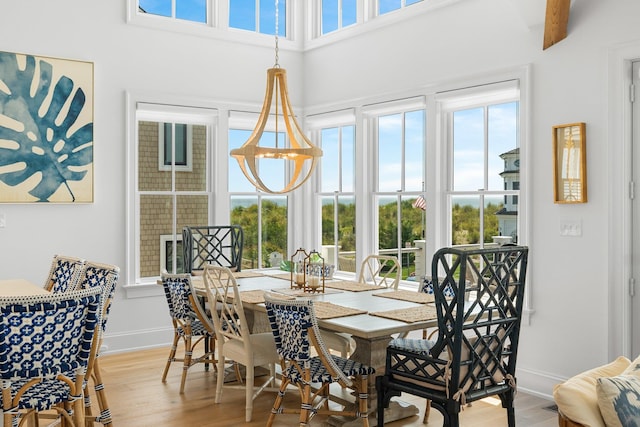 dining space with baseboards, light wood-type flooring, and a towering ceiling