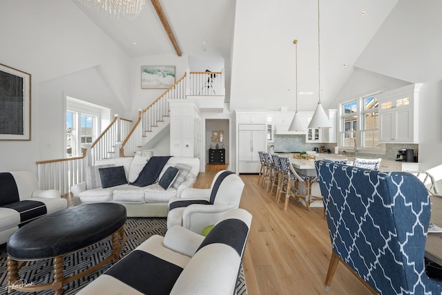 living room with stairs, beamed ceiling, light wood finished floors, and high vaulted ceiling