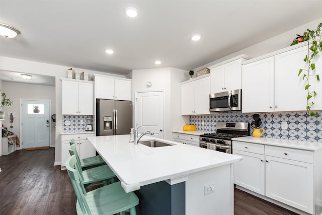 kitchen with sink, a kitchen island with sink, a breakfast bar, white cabinets, and appliances with stainless steel finishes