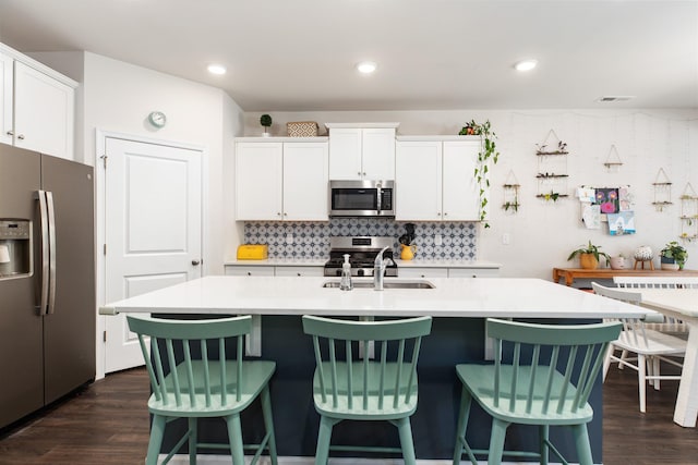 kitchen with sink, dark wood-type flooring, stainless steel appliances, a center island with sink, and white cabinets