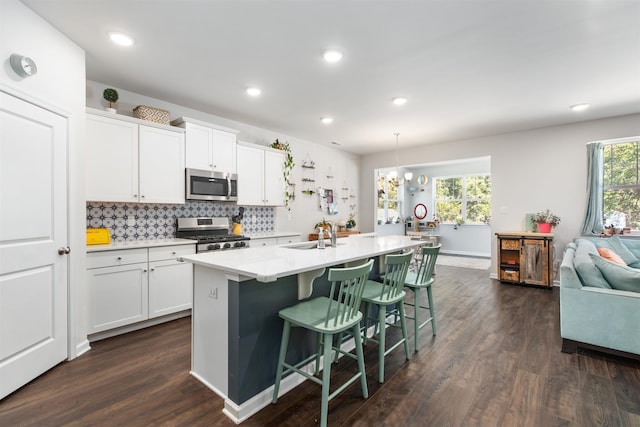 kitchen with sink, hanging light fixtures, a kitchen island with sink, white cabinets, and appliances with stainless steel finishes