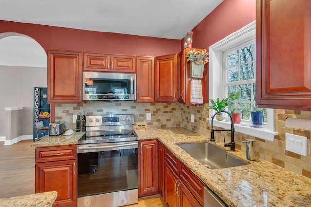 kitchen with light wood-type flooring, a sink, backsplash, appliances with stainless steel finishes, and light stone countertops