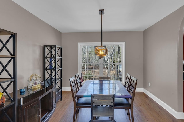 dining area with baseboards, arched walkways, and wood finished floors