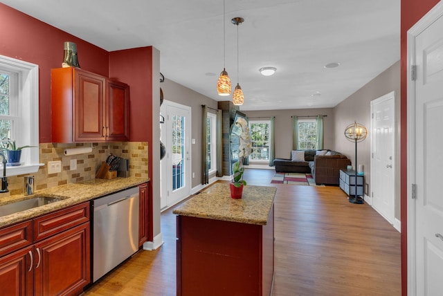 kitchen with light wood finished floors, tasteful backsplash, open floor plan, stainless steel dishwasher, and a sink