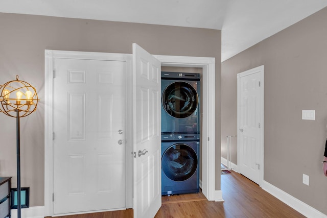 laundry area featuring baseboards, stacked washer and dryer, laundry area, an inviting chandelier, and wood finished floors