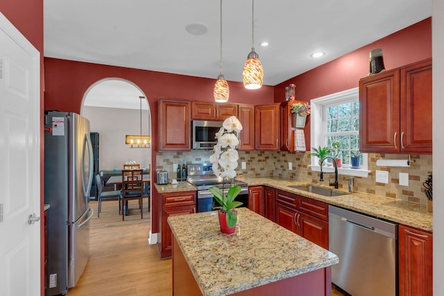 kitchen with a sink, stainless steel appliances, arched walkways, light wood-style floors, and hanging light fixtures