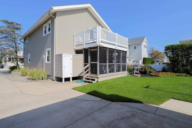 rear view of house with a balcony, a lawn, and a sunroom